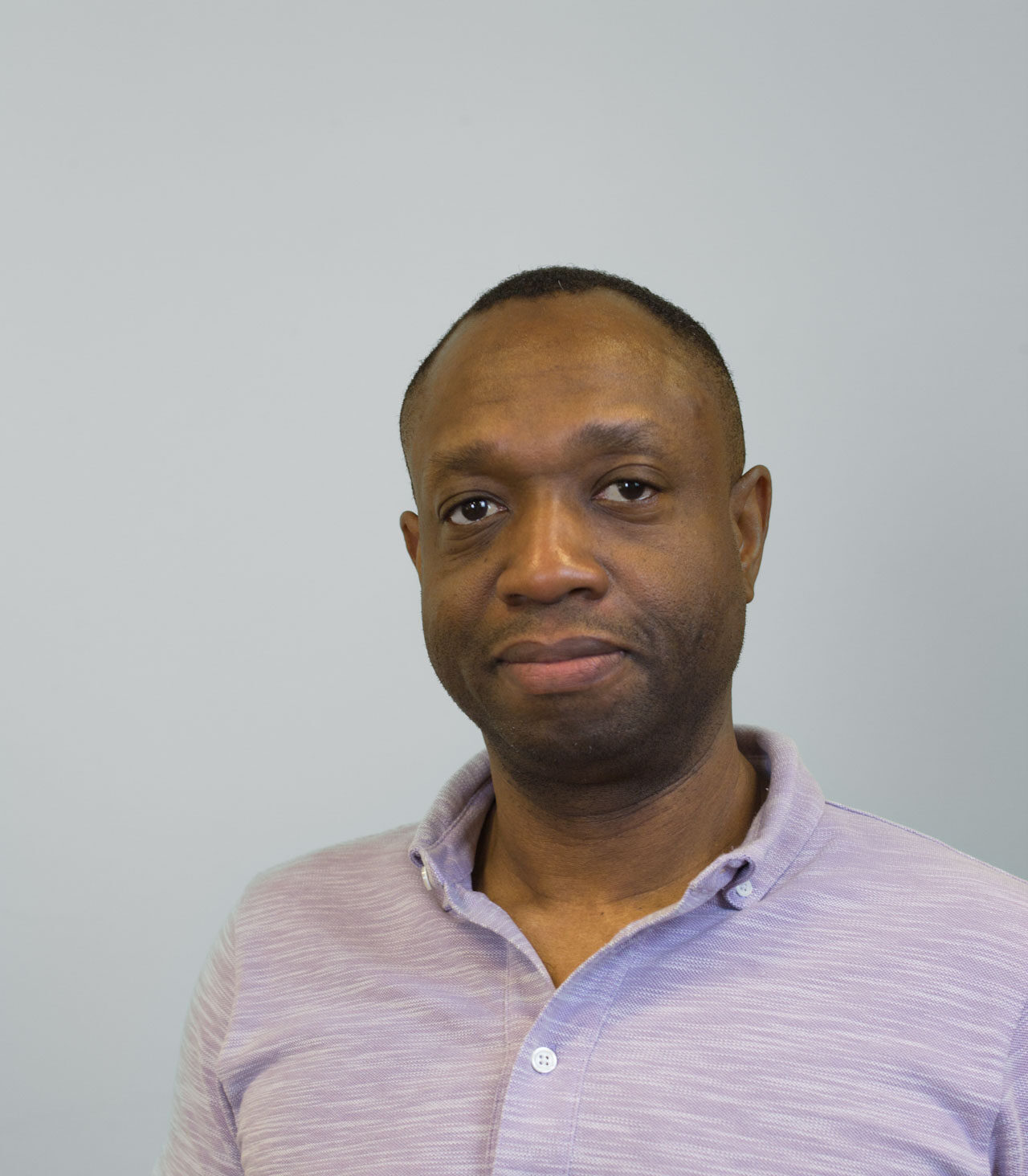 A headshot of Guy-Max Delphin against a neutral grey background.