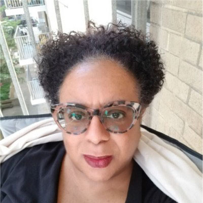 A headshot selfie of Eva-Marie Malone against an outdoor apartment balcony background.