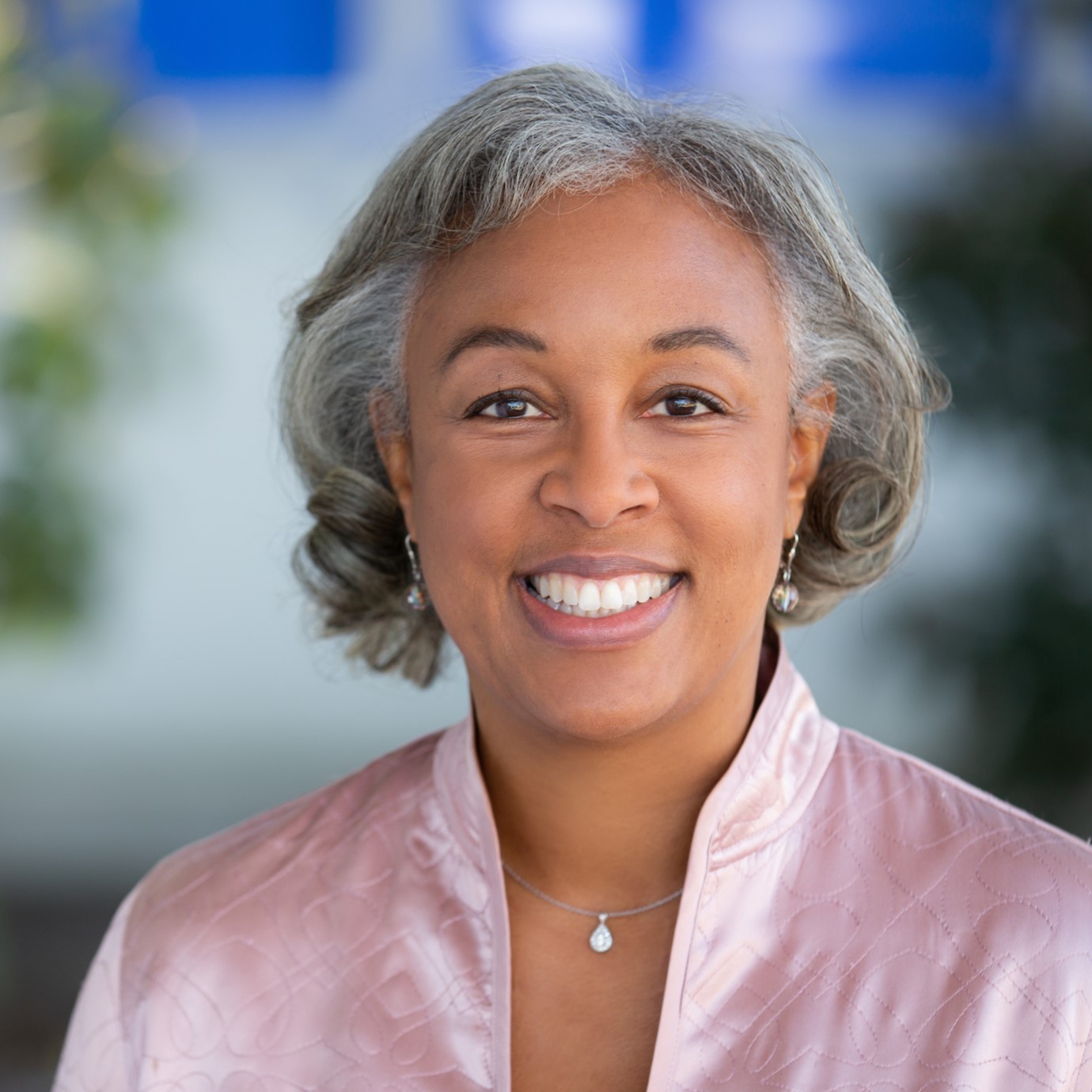 A headshot of Janis Smith-Gomez against a blurred outdoor background.