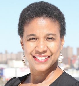 Headshot of Black woman with short hair against a blurred daytime cityscape.