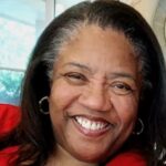 smiling black woman with mixed gray hair wearing a red top.