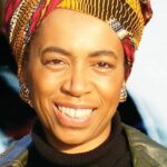 headshot of a smiling black woman wearing a colorful African print head wrap