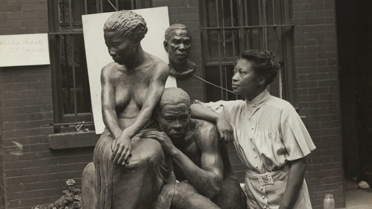 sculptor agusta savage standing to the right ans working of one of her pieces