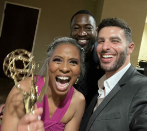 luchina fisher in a fuscia gown, and producers dwayne wade and jon marcus smile into the camera as she girps their emmy award trophy