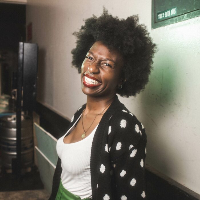 smiling black woman with an afro wearing a black and white polkadot jacket and white scoop neck top