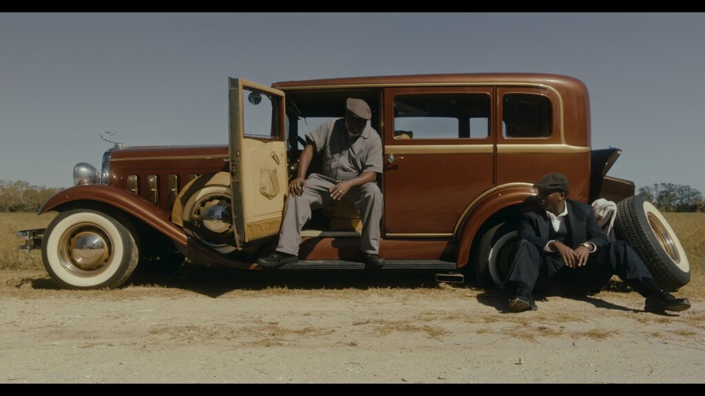 two men on the side of a road fixing the flat tire on a 1920's era sedan.