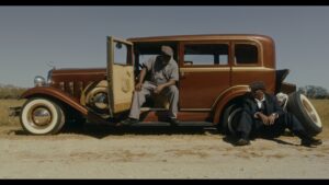 two men on the side of a road fixing the flat tire on a 1920's era sedan.